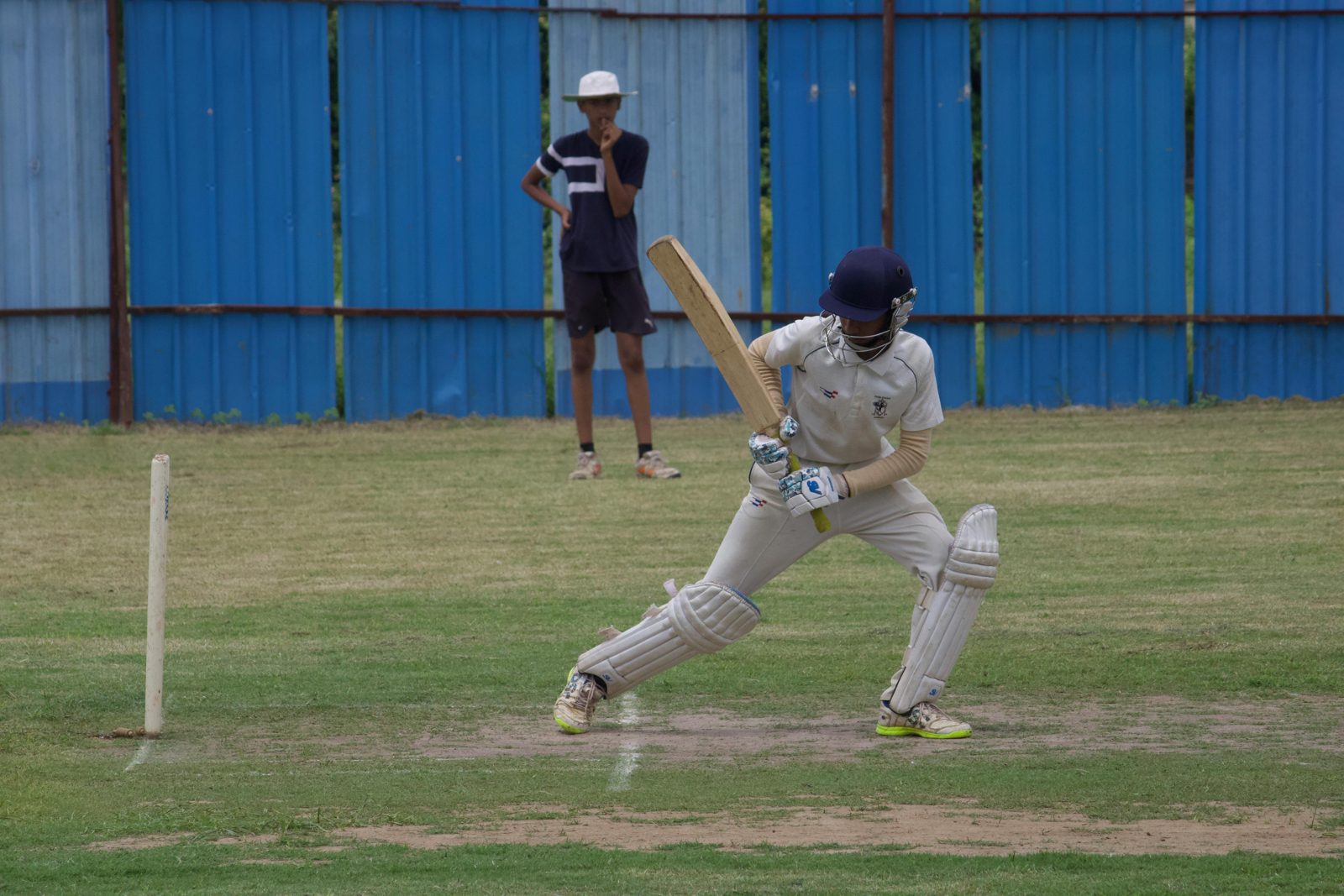 Young cricketer in white uniform batting on an outdoor cricket field